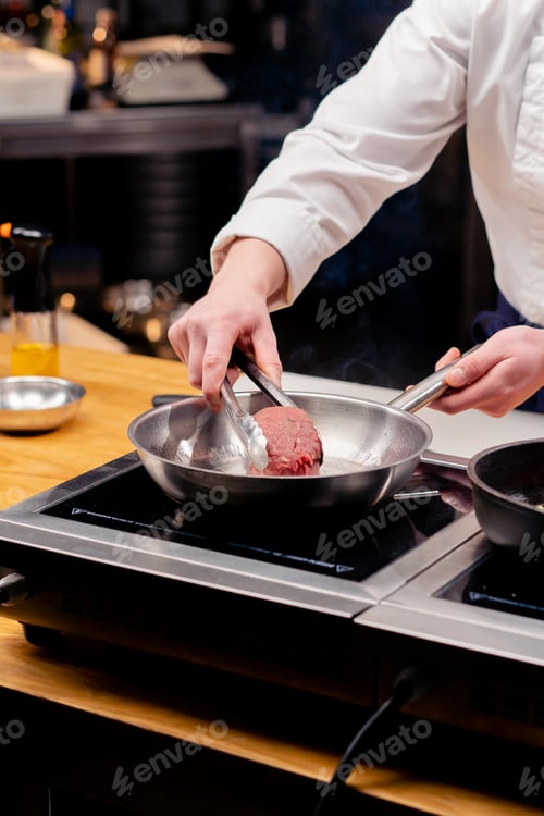 Preview: close-up of a chef's hand placing a beef steak on frying pan with tongs