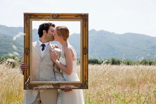 Preview: Newlyweds holding vintage picture frame, kissing