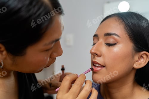 Preview: Professional makeup artist applying lip gloss to young latina
