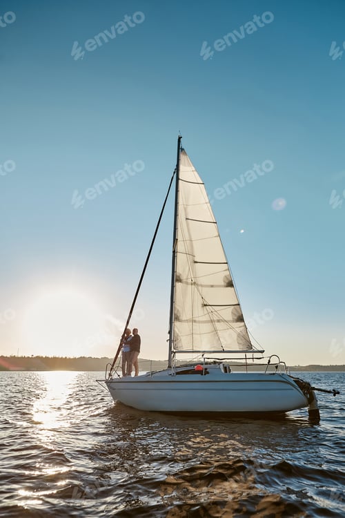 Preview: Romantic senior couple enjoying amazing sunset while standing on the side of sail boat or
