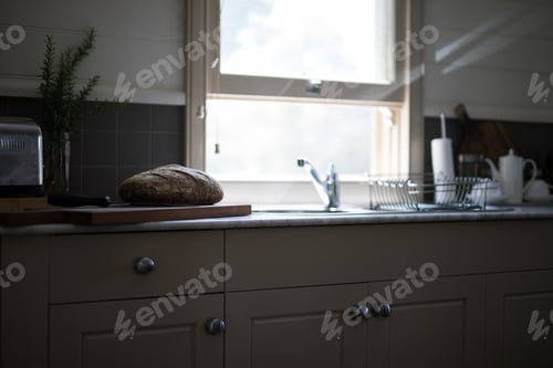 Preview: Rustic organic bread loaf on timber cutting board in kitchen lit by natural light