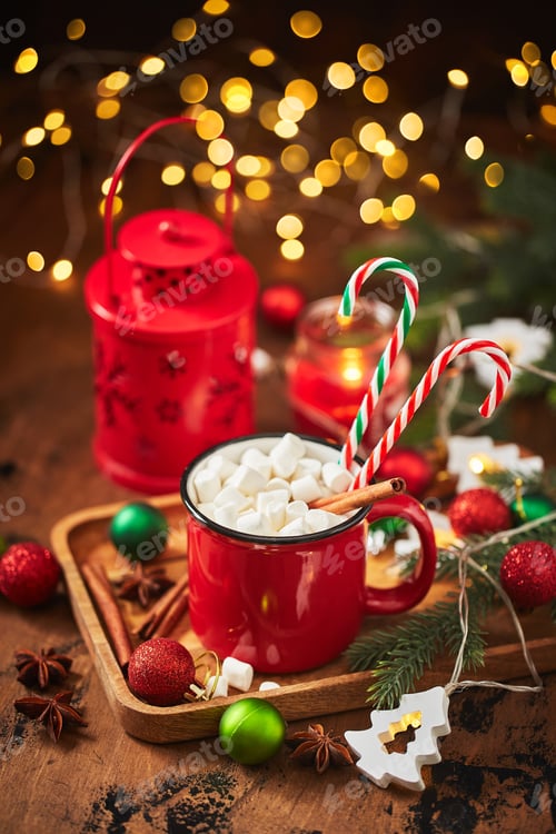 Preview: Red cup of hot cocoa with marshmallows and candy canes on wooden table with christmas tree and