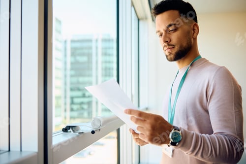 Preview: Young entrepreneur analyzing business report by his office window.