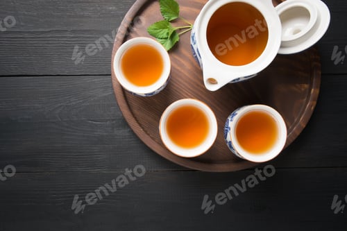 Preview: Cups of tea with melissa and kettle on dark background. Chinese tea concept. View from above.