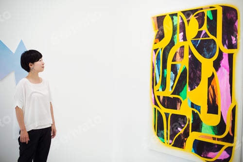 Preview: Woman with short black hair wearing white shirt standing in art gallery, looking at modern painting.