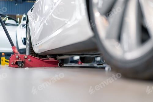 Preview: White luxury car being lifted with a red wheel change jack at a car service during detailing