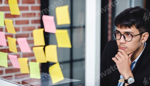 Preview: asian businessman looking and writing on sticky note for brainstorming ideas