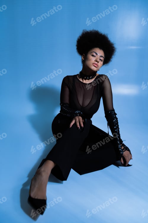 Preview: young african american woman in black veil looking at camera while sitting on blue
