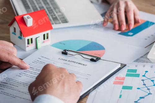 Preview: partial view of man reading loan agreement while sitting at desk with graphs and charts near