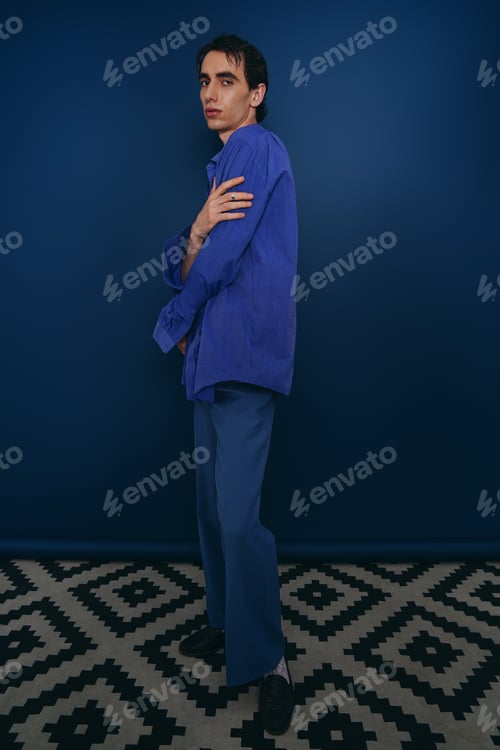 Preview: Handsome stylish man poses elegantly against a deep blue backdrop in modern fashion setting