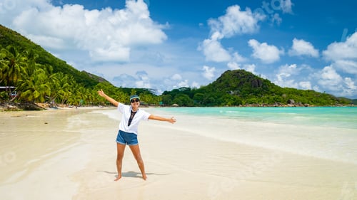 Preview: Young woman with hands up at a white tropical beach Anse Volbert beach Praslin Seychelles Islands.