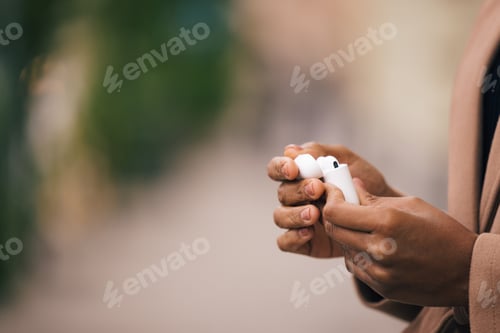 Preview: Close-Up of African American Hands Holding Wireless Earbuds Outdoors