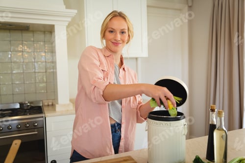 Preview: Portrait of smiling caucasian woman standing in kitchen preparing food, composting vegetable waste