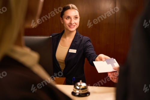 Preview: Smiling receptionist standing and giving keycard to hotel guest