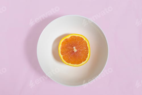 Preview: Flatlay over head shot of half of a blood orange in crisp white porcelain bowl on a soft pastel pink