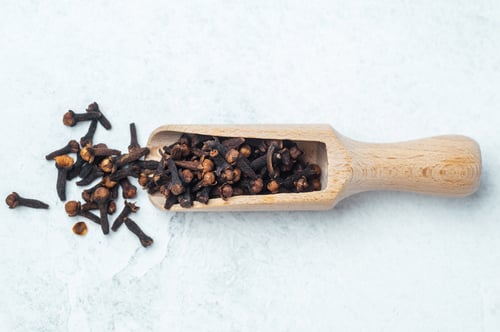 Preview: Cloves scattered next to a wooden scoop on a light surface