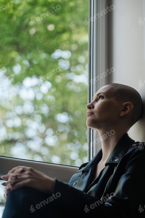 Preview: portrait of a young girl with a shaved head, she looks out the window