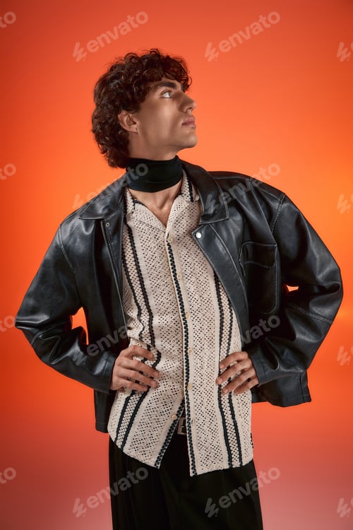 Preview: Stylish young man showcases modern fashion against vibrant orange backdrop