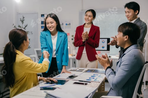 Preview: Two asian businesswomen shaking hands after closing a successful deal, while their colleagues are