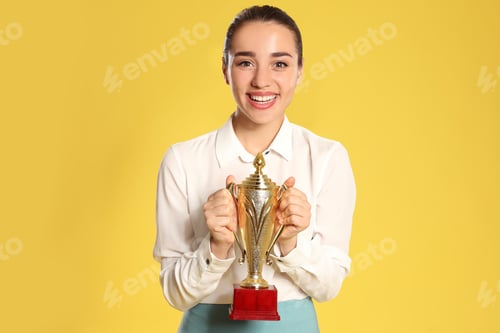 Preview: Portrait of happy young businesswoman with gold trophy cup on yellow background