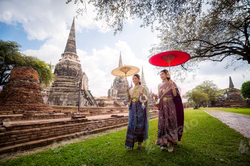 Preview: Asian beautiful wearing Thai traditional dress holding umbrella in ancient temple with old pagoda ba