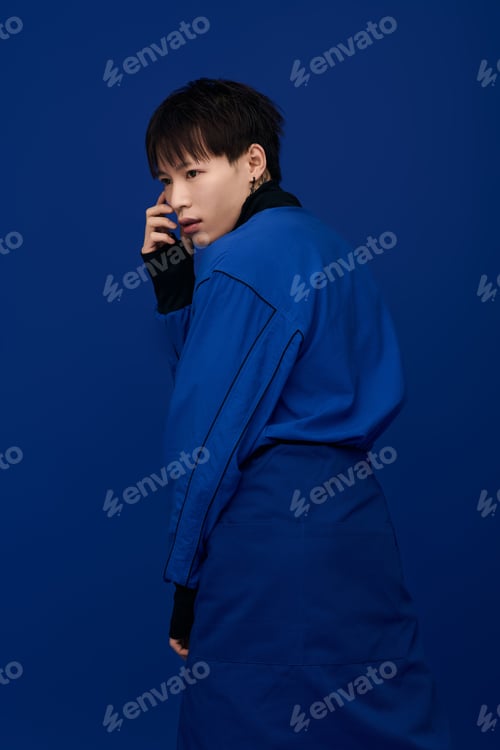 Preview: Young Asian man poses confidently against a vibrant blue background showcasing modern style
