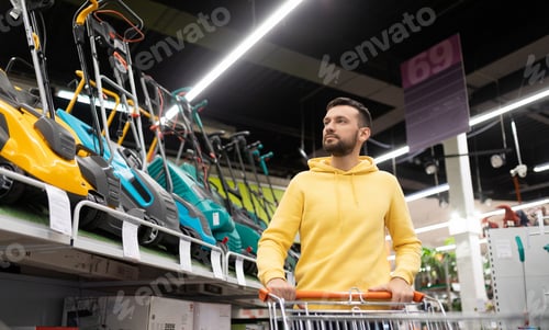 Preview: a man shopper walks with a trolley among the rows with a lawn mower me in a garden equipment store