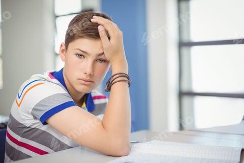 Preview: Teenage boy studying at desk in classroom with open workbook, gazing forward, copy space