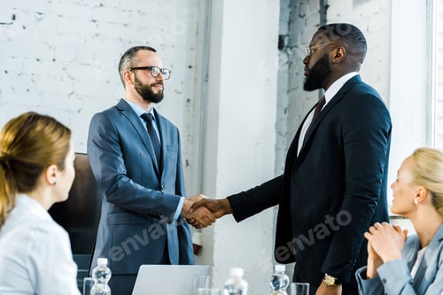 Preview: multicultural businessmen shaking hands near coworkers in office