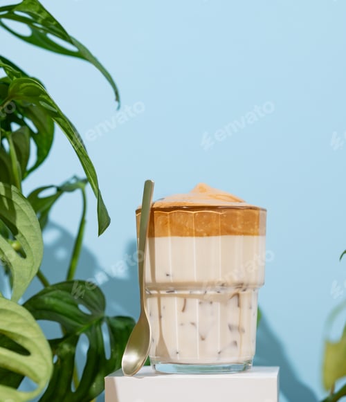 Preview: Dalgona coffee. Whipped instant coffee in a glass on a white stand with coffee beans