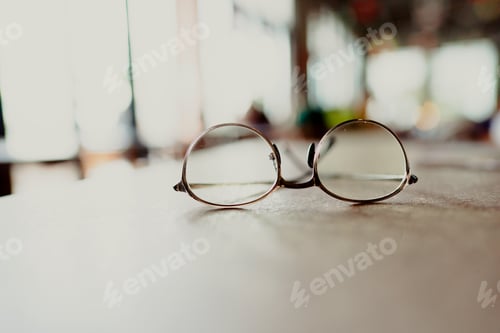 Preview: A pair of round eyeglasses with golden frames on reflective glass surface