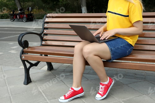 Preview: The girl works on a laptop while sitting on a bench