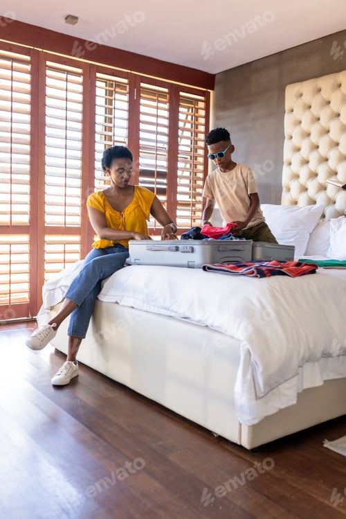 Preview: Mother and son packing suitcase on bed, preparing for family vacation