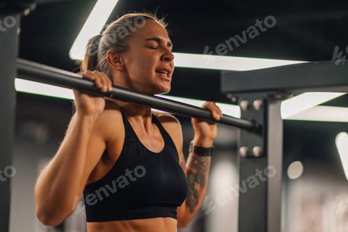 Preview: Determined sportswoman performing pull ups in modern gym setting