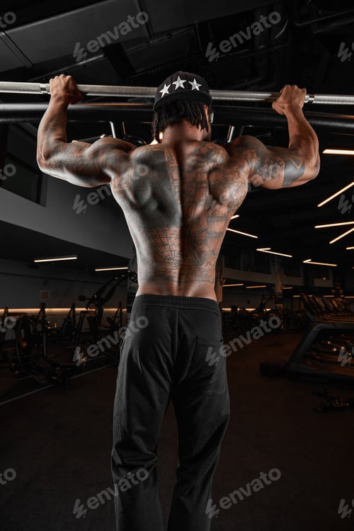 Preview: Strong and muscular dark skin man trains on modern equipment in gym. Portrait of muscular pumped up