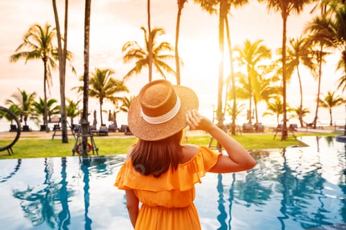 Preview: Young female relaxing and looking beautiful sunset over the sea at a tranquil tropical beach resort