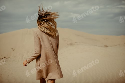 Preview: Woman walking across sand dunes with blowing hair