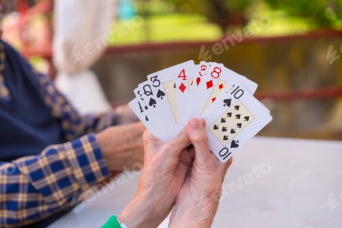 Preview: Hands of two elderly people in the garden of a nursing home or retirement home playing cards