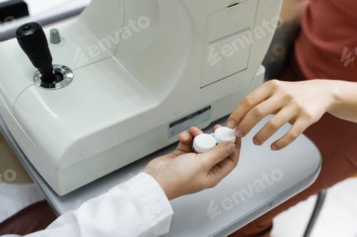 Preview: partial view of optometrist giving lens case to patient near autorefractor