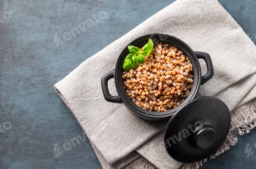 Preview: Buckwheat porridge with fresh herbs in a black pan on a napkin on a dark background.