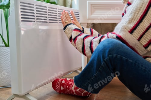 Preview: Close-up of woman hands legs warming near electric heating radiator