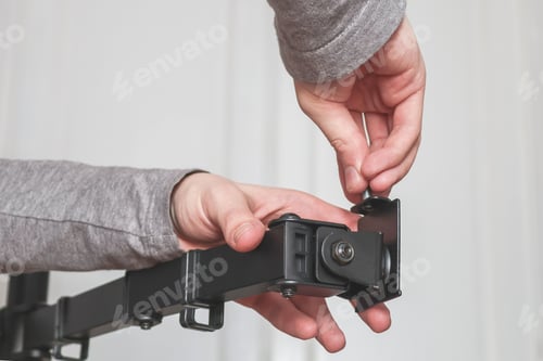 Preview: The hands of a young caucasian guy are twisting a bolt on a black bracket.
