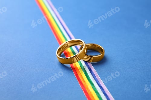 Preview: Wedding rings and rainbow ribbon on color background. Gay symbol