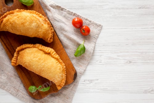 Preview: Homemade Deep Fried Italian Panzerotti Calzone on a rustic wooden board on a white wooden background