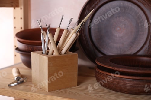 Preview: Set of different crafting tools and clay dishes on wooden rack in workshop