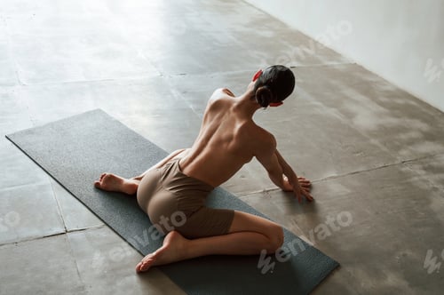 Preview: Sitting on yoga mat. Back view of sporty woman that is without bra indoors