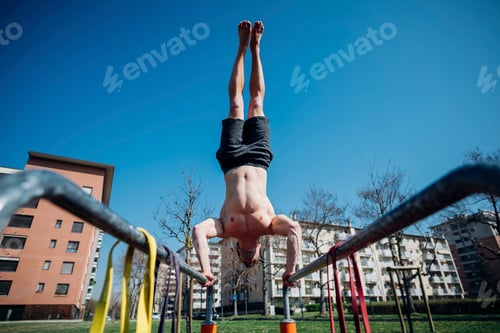 Preview: Calisthenics at outdoor gym, bare chested young man doing handstand on parallel bars, low angle view