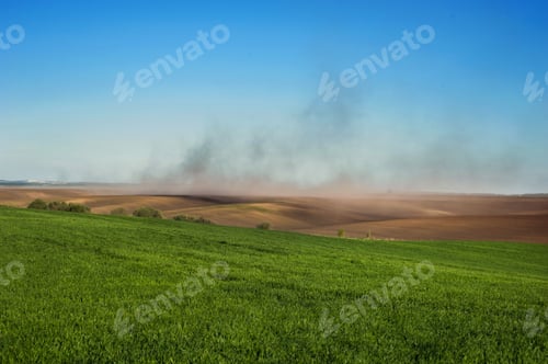 Preview: clouds of dust on the hills of plowed lands, green fields winter wheat and problem