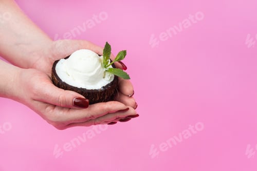 Preview: Vanilla ice cream balls in a fresh coconut half, decorated with mint leaves in your hand on a pink