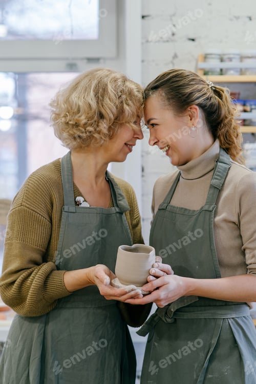 Preview: Elderly woman and young artisan holding handmade ceramic cup in pottery studio